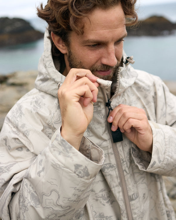 Man zipping a Vivida sherpa weatherproof changing robe Desert Sand by a lake