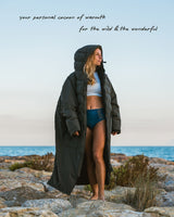 Woman keeping warm wearing Vivida's Best Premium Changing Robe in Black on a beach